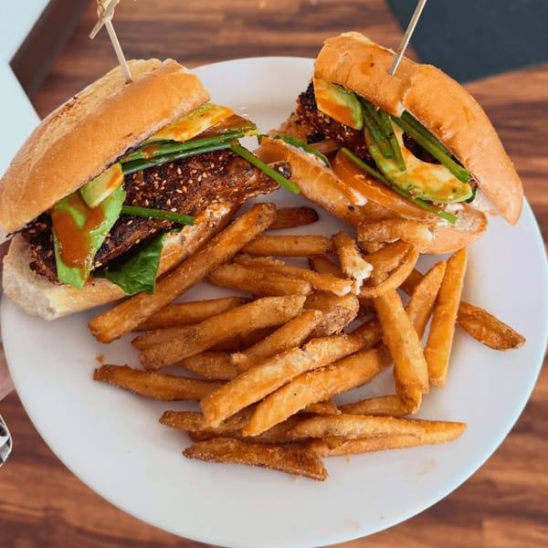 Two halves of a sandwich with avocado, greens, and sauce, served with a side of french fries.