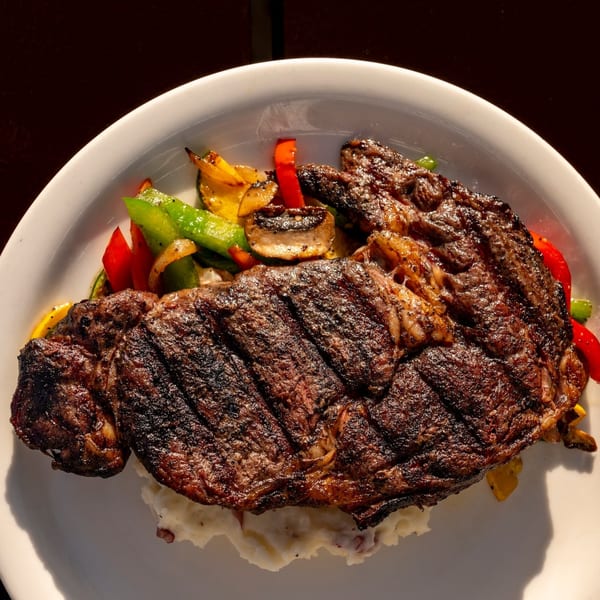 Grilled steak with grill marks, mashed potatoes, and colorful roasted vegetables on a white plate.