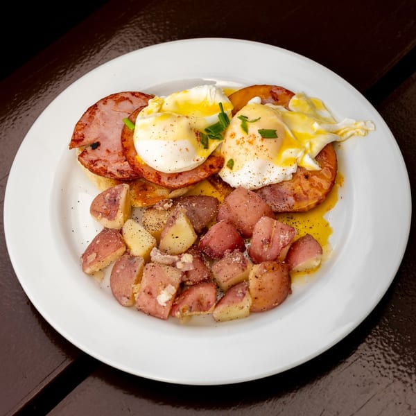 Breakfast plate with poached eggs, ham, and roasted red potatoes, garnished with chives and pepper.