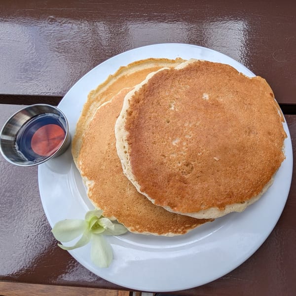 Golden pancakes on a white plate with a side of syrup and a white orchid.