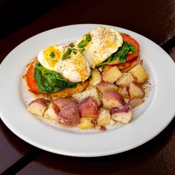 Eggs Benedict with spinach, tomato, and red potatoes on a white plate.