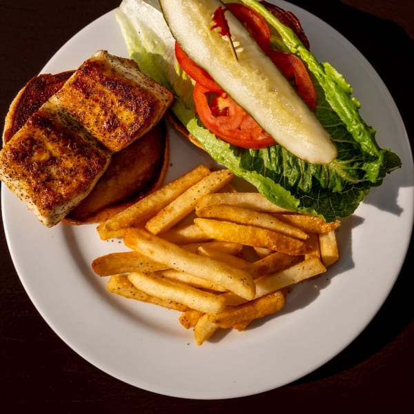 Grilled fish sandwich with lettuce, tomato, pickle, and a side of french fries on a white plate.