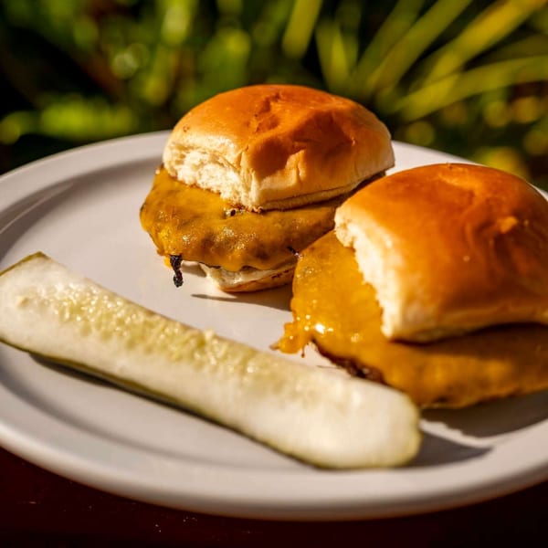 Two cheesy sliders with a pickle spear on a white plate, with a green background.